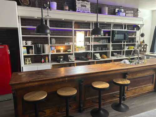 A modern kitchen with a wooden bar, stools, and shelves displaying kitchenware and decor.